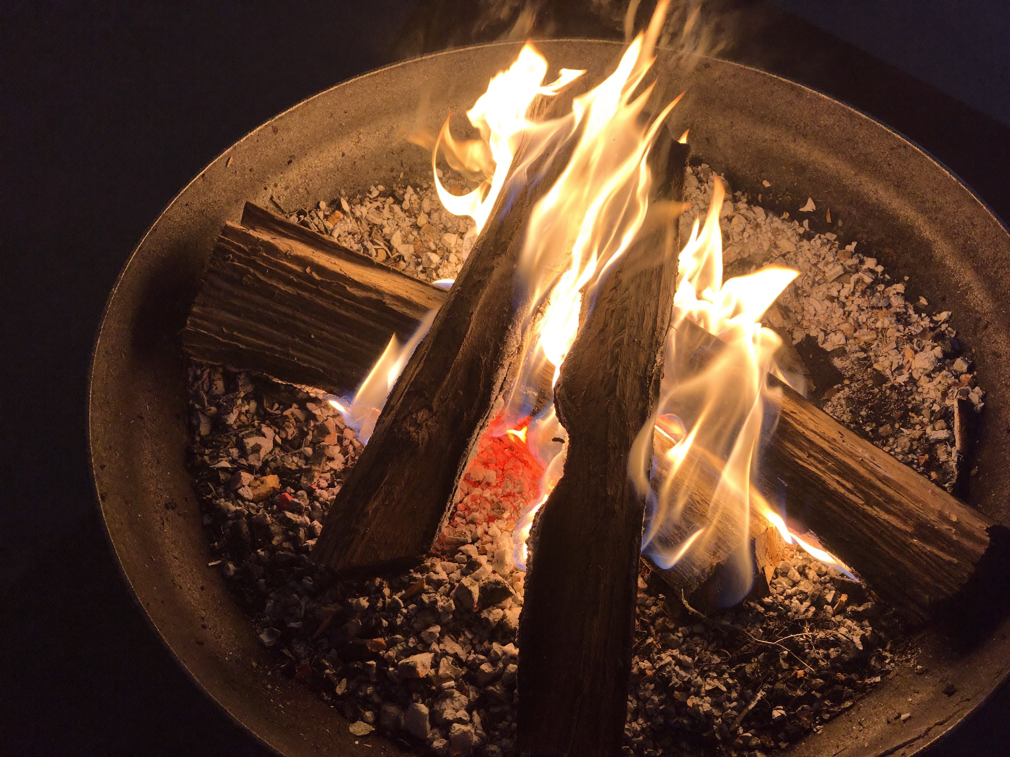 Dry seasoned split hardwood logs stacked next to a fire pit, the correct fuel for a clean burning fire.