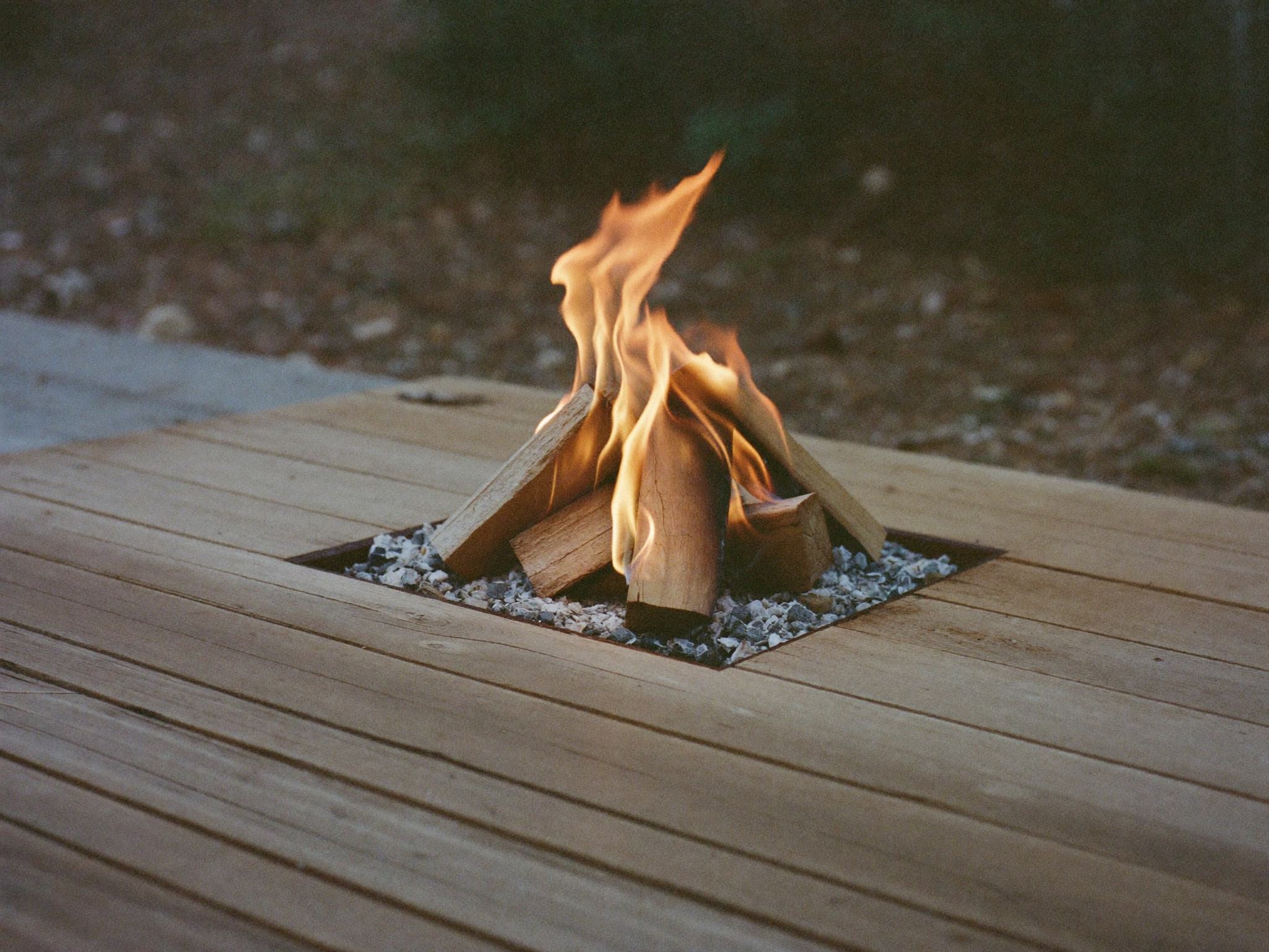 Log set burning in a fire pit bowl, radiating heat back toward the seating area