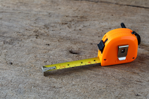 A yellow tape measure extended along the grass from the brick wall of a house to a round fire pit, showing a distance greater than 10 feet.