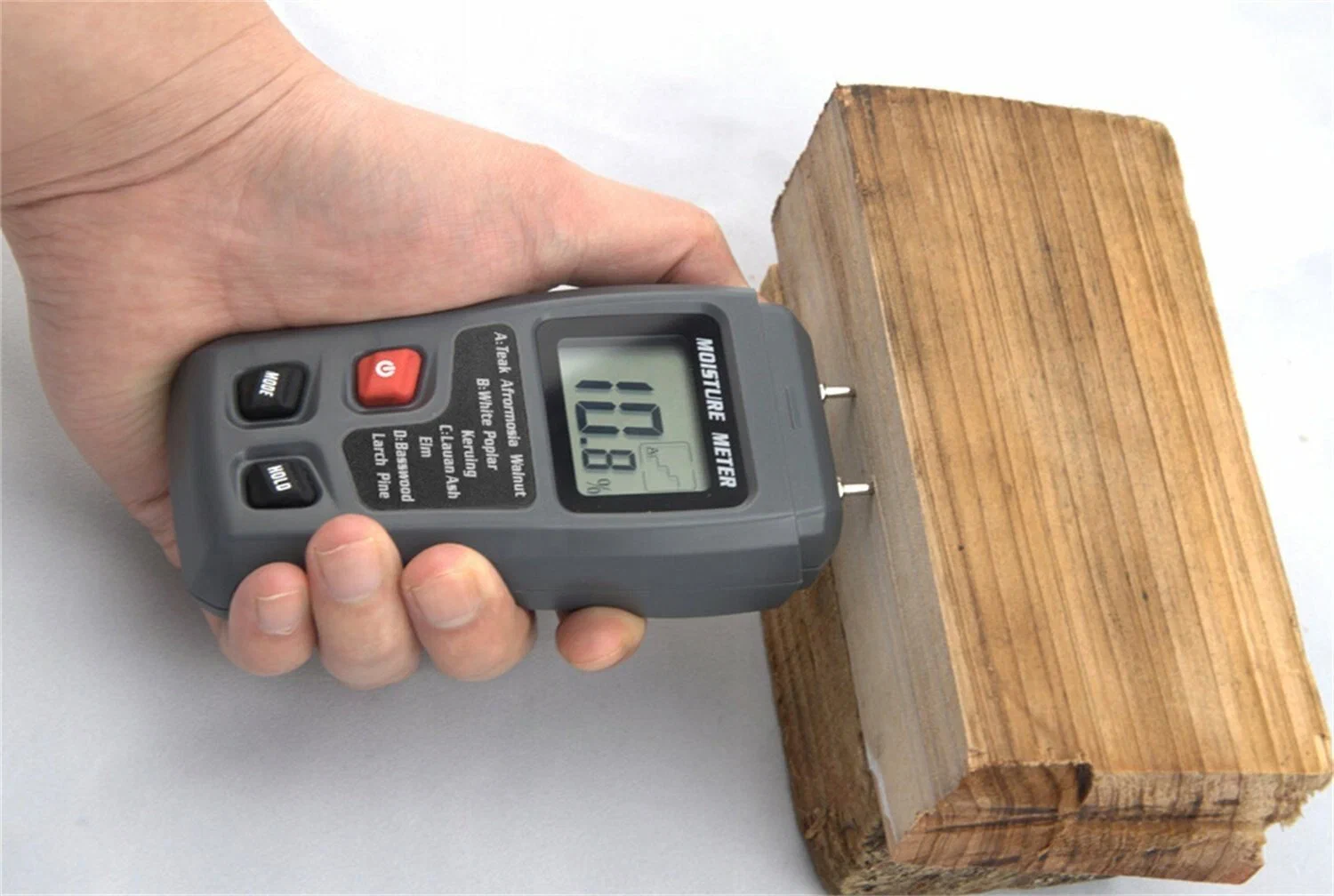 A digital wood moisture meter pressed against the split face of a log, showing a reading of 16.5 percent on its LCD screen.