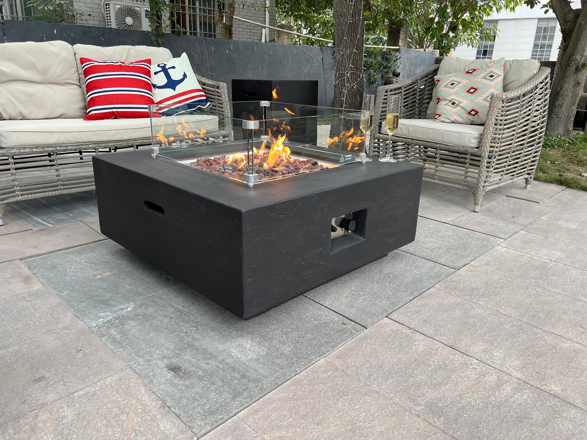 A propane gas fire table burning clean flames on a patio under a tall wooden pergola with open slats.