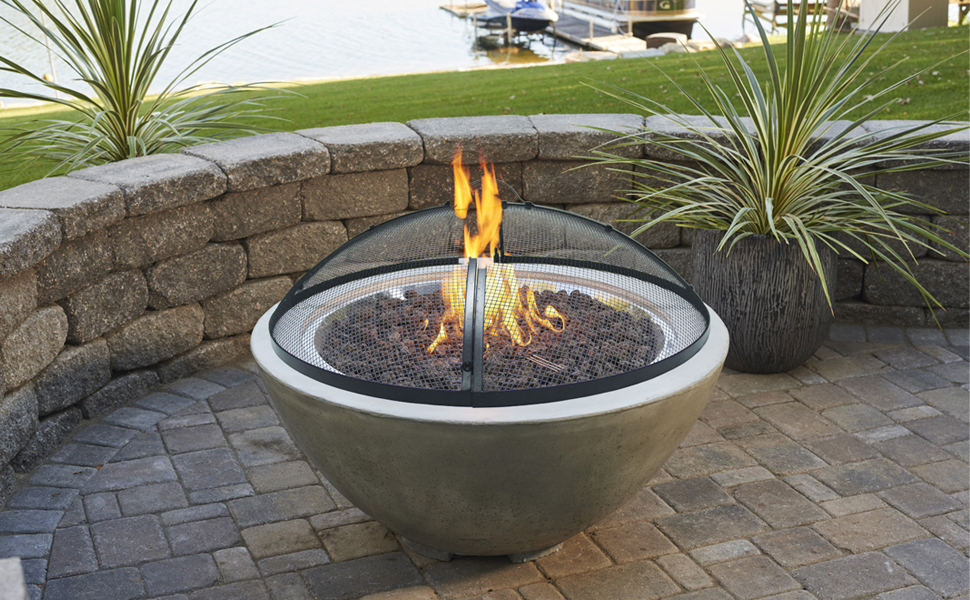 A round stainless steel mesh spark screen resting on top of an outdoor fire pit, preventing hot embers from escaping.