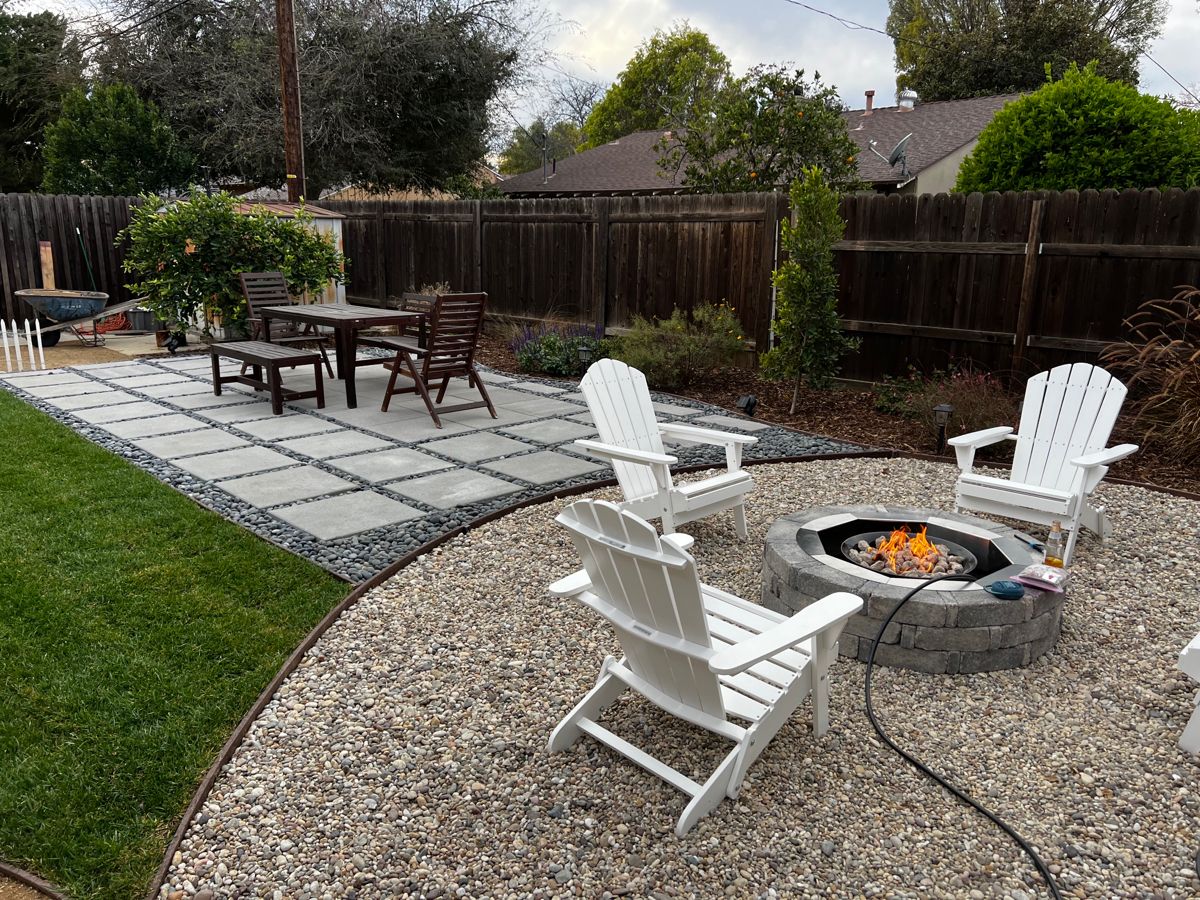 A wood burning fire pit sitting securely on a stone paver patio, surrounded by gravel borders and away from tree branches.