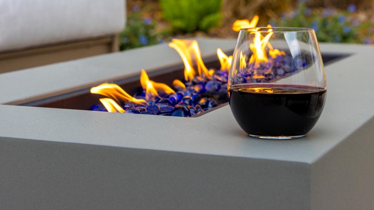 A stainless steel linear burner inside a black wicker fire table, surrounded by blue fire glass with a clean, low flame burning.