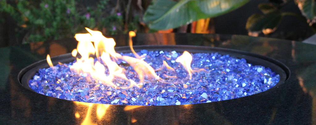A close-up of reflective cobalt-blue tempered fire glass beads sparkling under bright yellow flames in a modern gas fire table.
