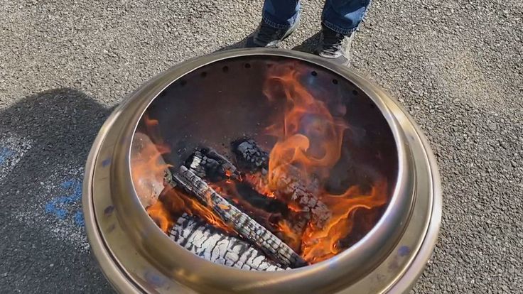A tight close-up showing bright yellow flames shooting from secondary combustion holes in a stainless steel smokeless fire pit.