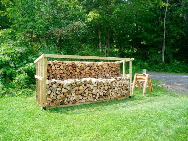 A neat stack of split oak firewood showing dry, seasoned logs with cracked end grain, piled outdoors in a wooden rack.