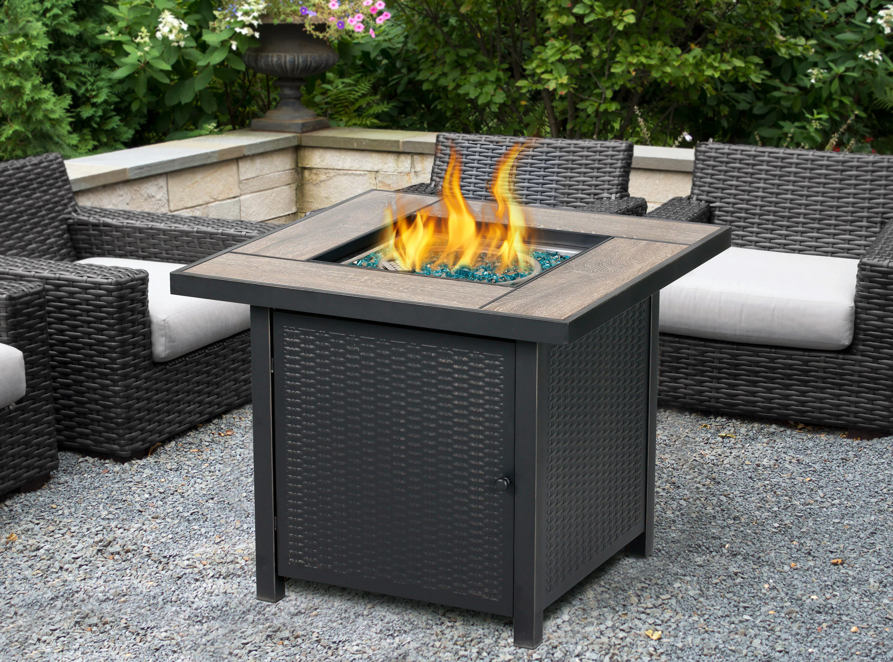 A standard white 20-pound propane cylinder sitting in the bottom slide-out drawer of a dark grey wicker gas fire table.