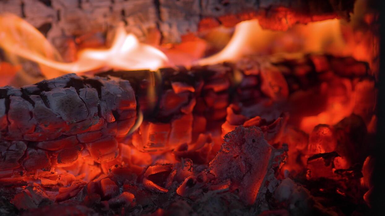 A thick, glowing bed of white-hot wood coals in a fire pit, with small wisps of smoke and no active flames, ready for cooking.